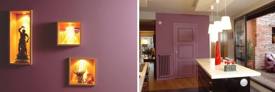 Niches lumineuses mettant en scène objets et sculptures sur mur aubergine, et cuisine ouverte à la porte parme donnant sur le patio