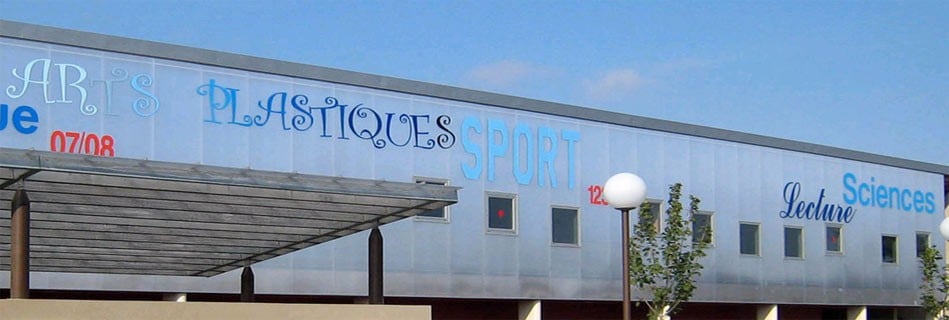 Façade en polycarbonate translucide portant les noms des disciplines, Arts plastiques, Sport, Sciences, Lecture, au-dessus d'un préau