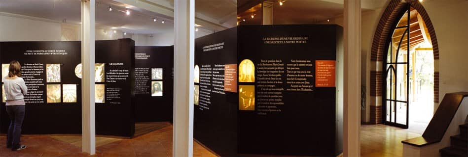 Parcours d'exposition aux panneaux noirs retraçant une vie, et porte cintrée en brique ouvrant sur l'auvent d'accès