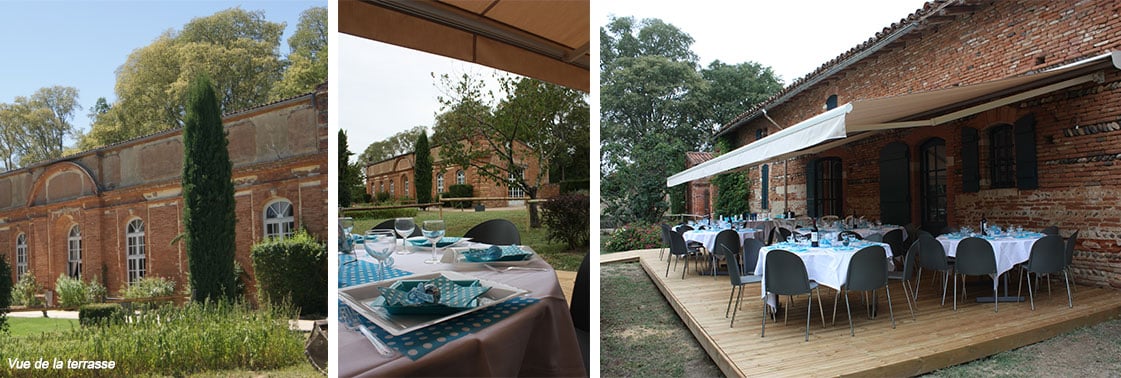 Vue de la terrasse : l'ancienne dépendance en brique du domaine, tables dressées pour une réception et terrasse en bois abritée d'un store