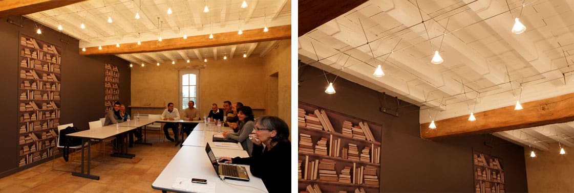 Salle de séminaire en configuration réunion avec guirlande d'ampoules, panneaux en trompe-l'œil de bibliothèque et plafond à poutres blanchies