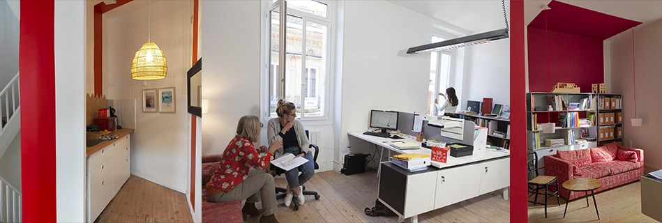 Kitchenette à encadrement rouge, coin d'échange autour d'un canapé et plateau de travail lumineux, et bibliothèque rouge et matériauthèque