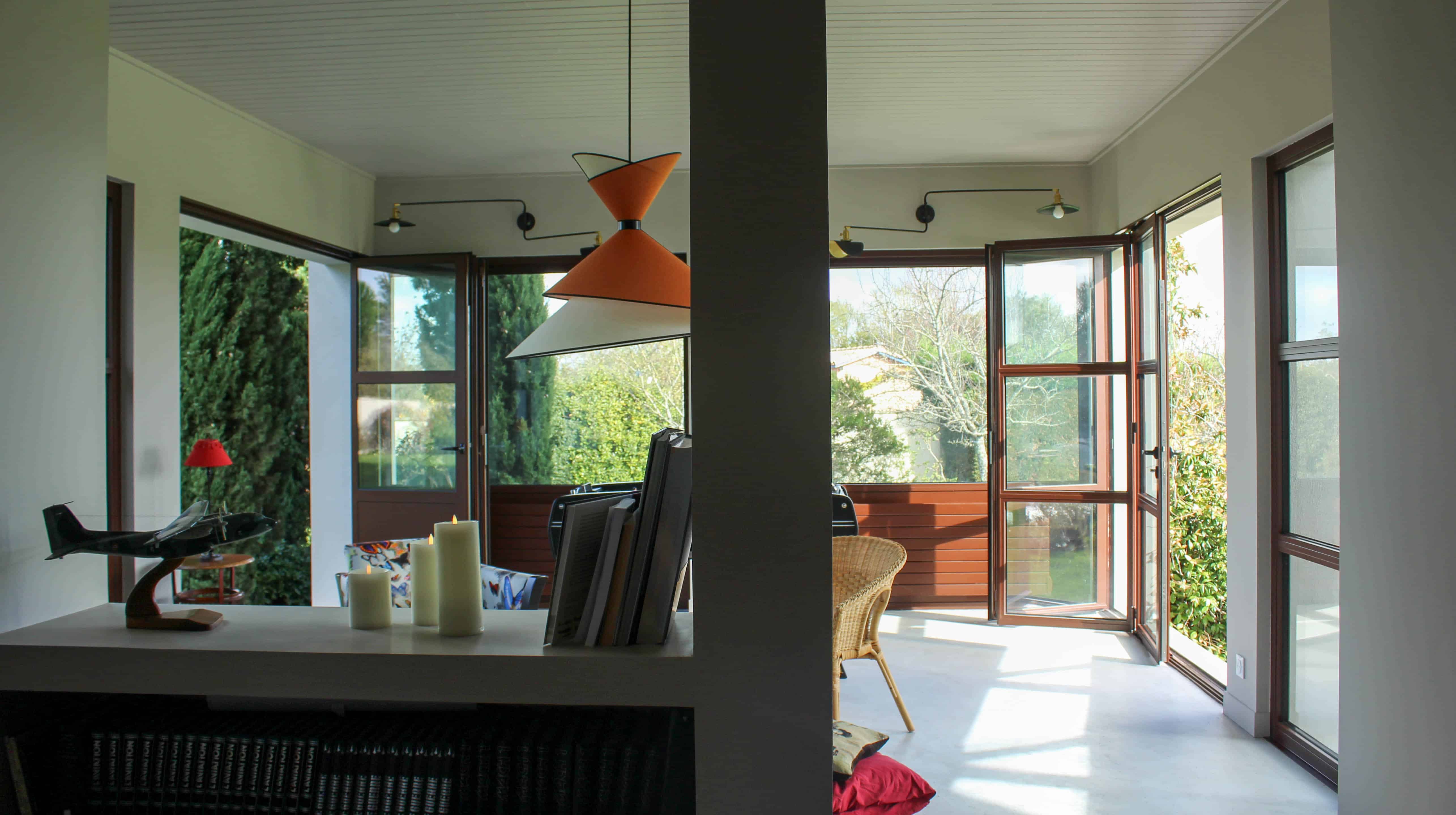 Nouvelle pièce à vivre créée sous la terrasse couverte, baies vitrées bois ouvertes sur le jardin et suspension orange au plafond lambrissé